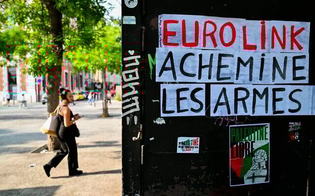 Un piéton devant des pancartes sur lesquelles on peut lire "Eurolink achemine les armes" et "Palestine libre" lors d'un rassemblement contre une cargaison de pièces d'équipement militaire destinées à Israël, à Marseille, le 5 juin 2025. (Crédit : Christophe Simon/AFP)