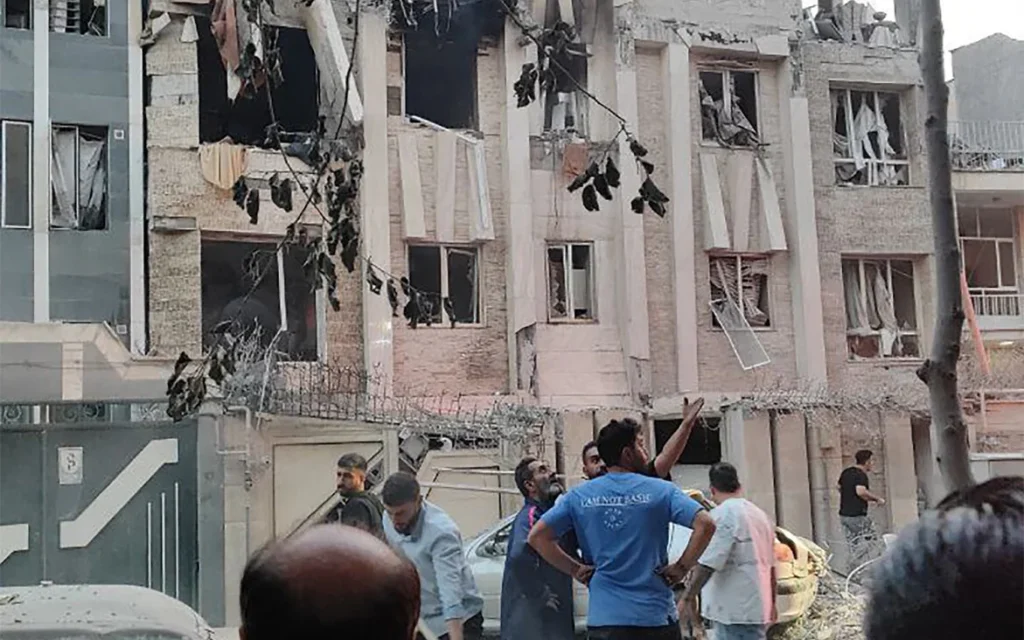 Cette photo publiée par la chaîne Telegram officielle Sepah News du Corps des gardiens de la révolution islamique iranienne (CGRI) le 13 juin 2025 montre des personnes regardant un bâtiment endommagé à la suite d'une frappe israélienne sur la capitale iranienne Téhéran (Crédit : SEPAH NEWS/AFP)
