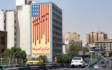 Des véhicules circulant sur le pont Karim Khan Zand, dans le centre-ville de Téhéran, passent devant la fresque « À bas les États-Unis » peinte sur le mur du bâtiment de l'Organisation nationale des examens éducatifs, le 13 juin 2025. (Crédit : AFP)