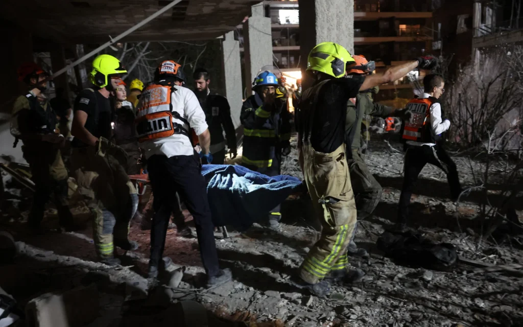 Les premiers secours évacuant une victime d'un immeuble touché par un missile tiré depuis l'Iran, à Ramat Gan près de Tel Aviv, le 13 juin 2025. (Crédit : Jack Guez/AFP)