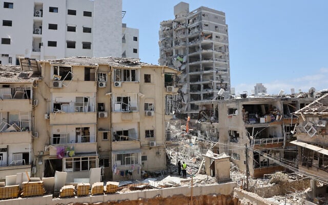 Les secours israéliens se tiennent au milieu des décombres de bâtiments fortement endommagés, après une frappe de missiles iraniens dans la nuit du 15 juin 2025, à Bat Yam. (Crédit :  GIL COHEN-MAGEN / AFP)