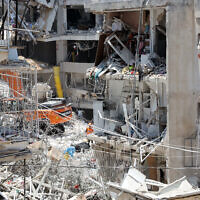 Les secours israéliens se tiennent au milieu des décombres de bâtiments fortement endommagés, après une frappe de missiles iraniens dans la nuit du 15 juin 2025, à Bat Yam. (Crédit :  GIL COHEN-MAGEN / AFP)
