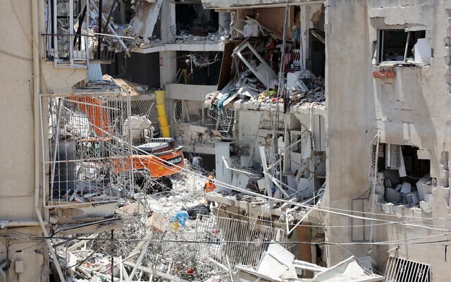 Les secours israéliens se tiennent au milieu des décombres de bâtiments fortement endommagés, après une frappe de missiles iraniens dans la nuit du 15 juin 2025, à Bat Yam. (Crédit :  GIL COHEN-MAGEN / AFP)