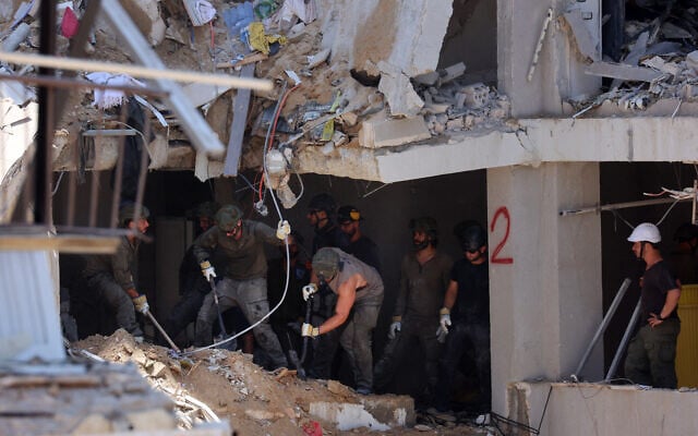 Les secours israéliens se tiennent au milieu des décombres de bâtiments fortement endommagés, après une frappe de missiles iraniens dans la nuit du 15 juin 2025, à Bat Yam. (Crédit :  GIL COHEN-MAGEN / AFP)