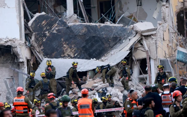 Les sauveteurs fouillent les décombres d'un bâtiment endommagé dans le centre d'Israël après une nouvelle salve de roquettes iraniennes le 16 juin 2025. (Crédit : Menahem Kahana / AFP)
