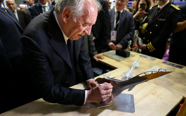 Le Premier ministre français François Bayrou signe une maquette d'un avion de combat Rafale lors de la 55e édition du Salon international de l'aéronautique et de l'espace au parc des expositions du Bourget, à Paris, le 16 juin 2025. (Crédit : ALAIN JOCARD / POOL / AFP)