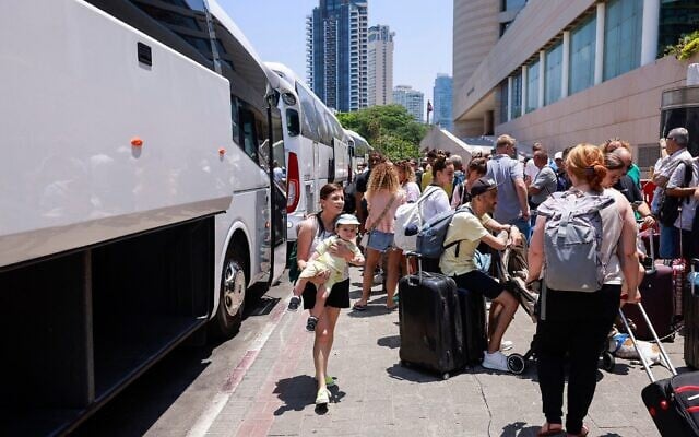 Des personnes attendent avec leurs bagages le départ d'un bus prévu pour évacuer les détenteurs de passeports étrangers, principalement des Européens, hors d'Israël, à un point de rendez-vous à Tel Aviv le 17 juin 2025. L'opération, coordonnée par l'ambassade de Pologne, vise à évacuer plusieurs centaines de personnes qui monteront dans des bus à destination du Sinaï en Égypte, et de là continueront vers Varsovie, en Pologne. (Crédit : Menahem Kahana/AFP)
