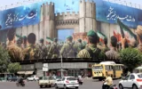 Des véhicules passent devant une banderole anti-israélienne représentant des soldats iraniens se dirigeant vers le territoire israélien sur la place Enghelab (Révolution), à Téhéran, le 24 juin 2025 (Crédit : ATTA KENARE/AFP)