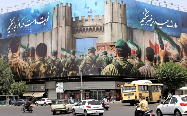 Des véhicules passent devant une banderole anti-israélienne représentant des soldats iraniens se dirigeant vers le territoire israélien sur la place Enghelab (Révolution), à Téhéran, le 24 juin 2025 (Crédit : ATTA KENARE/AFP)