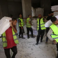 Des volontaires transportent des sacs de farine destinés à être distribués aux Palestiniens dans un dépôt mis en place par l'organisation indépendante Save Youth Future Society (SYFS), en coordination avec le Programme alimentaire mondial (PAM) de l'ONU, dans la ville de Gaza, le 26 juin 2025. (Crédit : BASHAR TALEB / AFP)