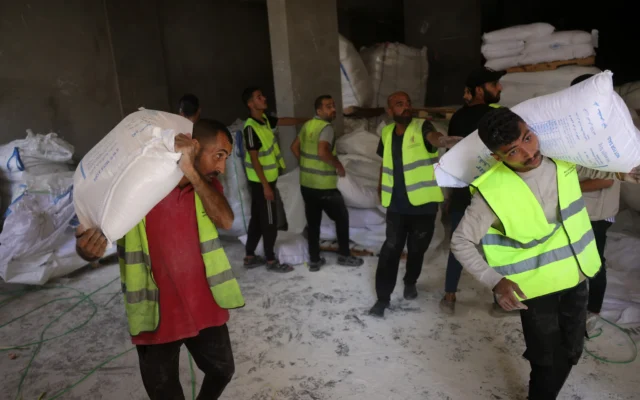 Des volontaires transportent des sacs de farine destinés à être distribués aux Palestiniens dans un dépôt mis en place par l'organisation indépendante Save Youth Future Society (SYFS), en coordination avec le Programme alimentaire mondial (PAM) de l'ONU, dans la ville de Gaza, le 26 juin 2025. (Crédit : BASHAR TALEB / AFP)