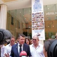 Le maire de Nice, Christian Estrosi (C), s'adresse à la presse à côté d'une banderole affichant des photos d'otages israéliens détenus par le Hamas et d'un couple français détenu en Iran, après qu'un tribunal administratif a ordonné le retrait des drapeaux israéliens du balcon de l'hôtel de ville, à Nice, dans le sud de la France, le 26 juin 2025. (Crédit : Valery HACHE / AFP)
