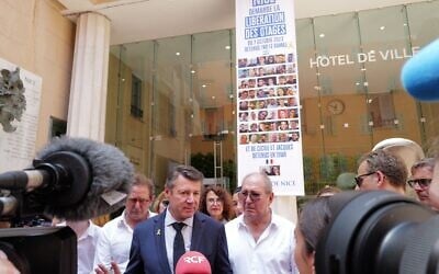 Le maire de Nice, Christian Estrosi (C), s'adresse à la presse à côté d'une banderole affichant des photos d'otages israéliens détenus par le Hamas et d'un couple français détenu en Iran, après qu'un tribunal administratif a ordonné le retrait des drapeaux israéliens du balcon de l'hôtel de ville, à Nice, dans le sud de la France, le 26 juin 2025. (Crédit : Valery HACHE / AFP)