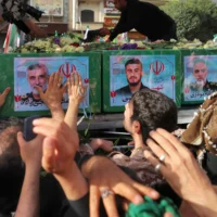 Des personnes en deuil se tenant près du cercueil du commandant du Corps des Gardiens de la Révolution islamique (CGRI) Amir Ali Hjizadeh (à gauche) et d'autres commandants militaires tués lors des frappes israéliennes le premier jour de la guerre, lors de leur cortège funèbre, sur la place Enqelab dans la capitale de Téhéran, le 28 juin 2025. (Crédit : Atta Kenare/AFP)