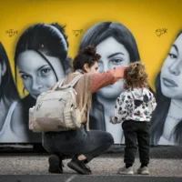 Une femme et une petite fille regardent une peinture murale représentant des soldates israéliennes prises en otage lors du pogrom du 7 octobre 2023 menée par le Hamas contre Israël, à Tel Aviv, le 18 janvier 2025. (Crédit : Oded Balilty/AP)