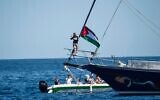 L'activiste pour le climat Greta Thunberg se tenant près d'un drapeau palestinien, après être montée à bord du Madleen et avant de mettre le cap sur Gaza avec des activistes de la Freedom Flottilla Coalition au départ du port sicilien de Catane, en Italie, le 1ᵉʳ juin 2025. (Crédit : Salvatore Cavalli/AP)