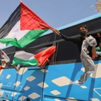 Des membres du convoi, dont des militants et des sympathisants algériens et tunisiens, agitent des drapeaux palestiniens depuis un bus alors que le groupe se dirige vers Gaza via le point de passage égyptien de Rafah, à Zawiya, en Libye, le 10 juin 2025. (Crédit : AP Photo/Yousef Murad)