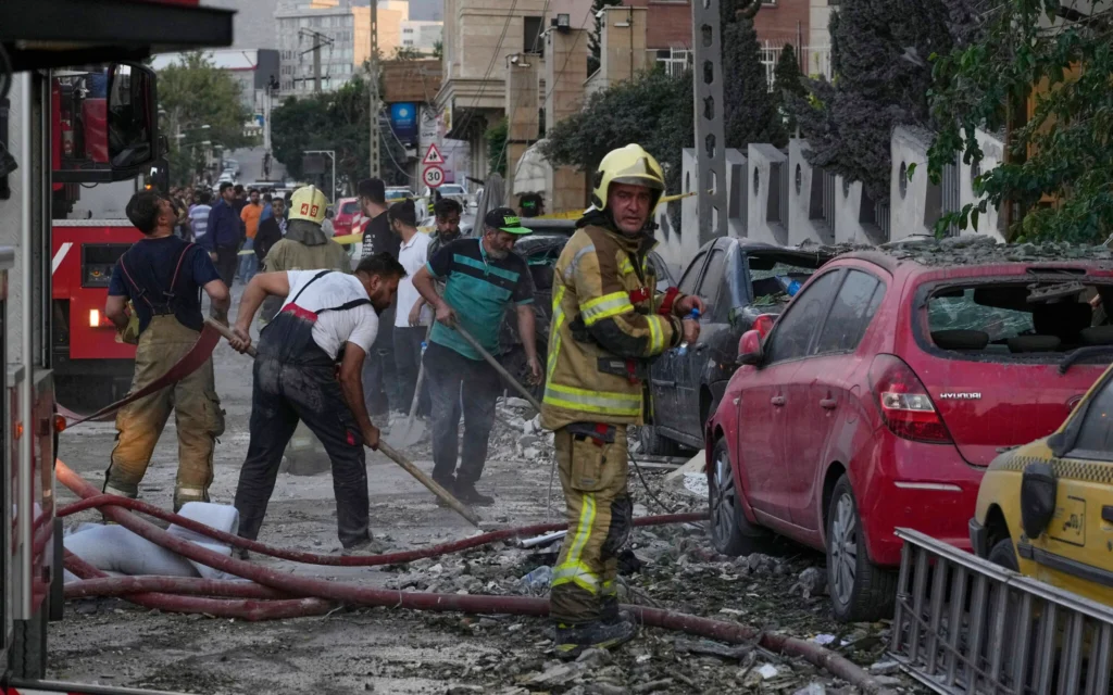 Des pompiers et des habitants nettoyant les lieux d'une explosion dans un complexe résidentiel après des frappes israéliennes à Téhéran, le 13 juin 2025. (Crédit : Vahid Salemi/AP)