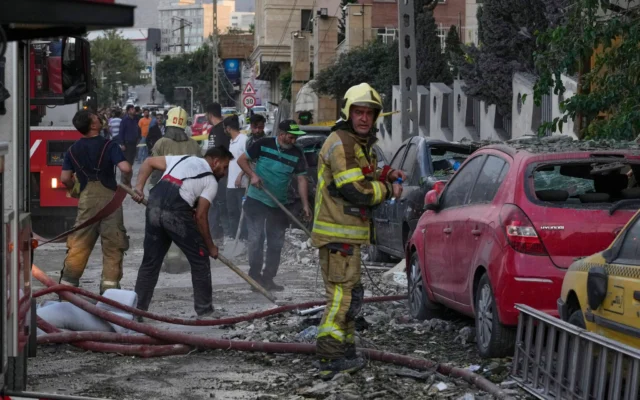 Des pompiers et des habitants nettoyant les lieux d'une explosion dans un complexe résidentiel après des frappes israéliennes à Téhéran, le 13 juin 2025. (Crédit : Vahid Salemi/AP)