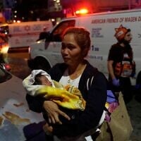 Une femme tenant un bébé dans ses bras évacue les lieux après qu'un missile lancé depuis l'Iran a frappé Tel Aviv, le 16 juin 2025. (Crédit : Baz Ratner/AP)