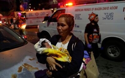 Une femme tenant un bébé dans ses bras évacue les lieux après qu'un missile lancé depuis l'Iran a frappé Tel Aviv, le 16 juin 2025. (Crédit : Baz Ratner/AP)
