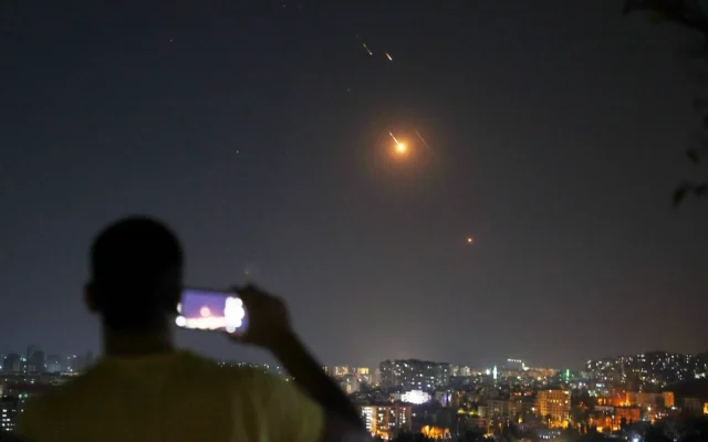 Un homme prenant une photo avec son téléphone portable alors que des missiles tirés depuis l'Iran en direction d'Israël survolent le territoire syrien, à Damas, en Syrie, le 18 juin 2025. (Crédit : Ghaith Alsayed/AP)