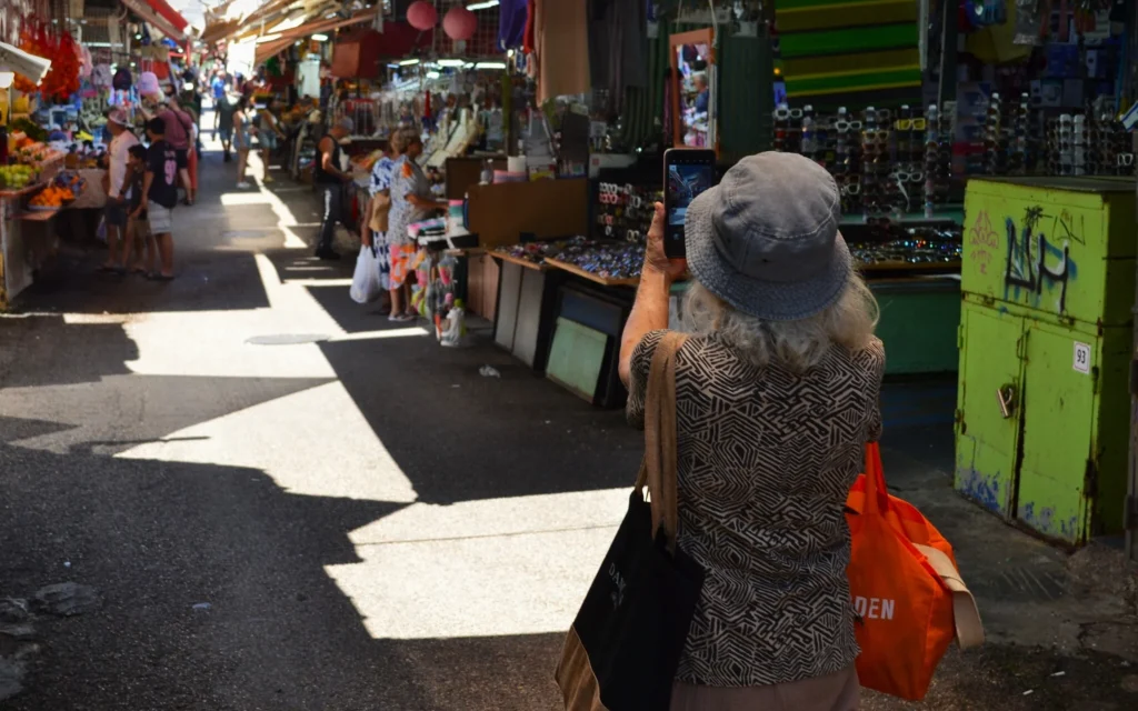 Une femme s’arrête pour prendre une photo du Shuk HaCarmel à Tel Aviv, un jour après l’annonce d’un cessez-le-feu entre Israël et l’Iran, le 25 juin 2025. (Crédit : Stav Levaton/Times of Israel)