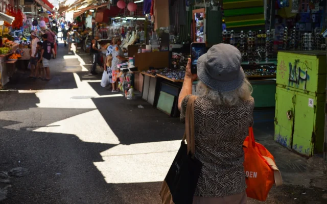Une femme s’arrête pour prendre une photo du Shuk HaCarmel à Tel Aviv, un jour après l’annonce d’un cessez-le-feu entre Israël et l’Iran, le 25 juin 2025. (Crédit : Stav Levaton/Times of Israel)