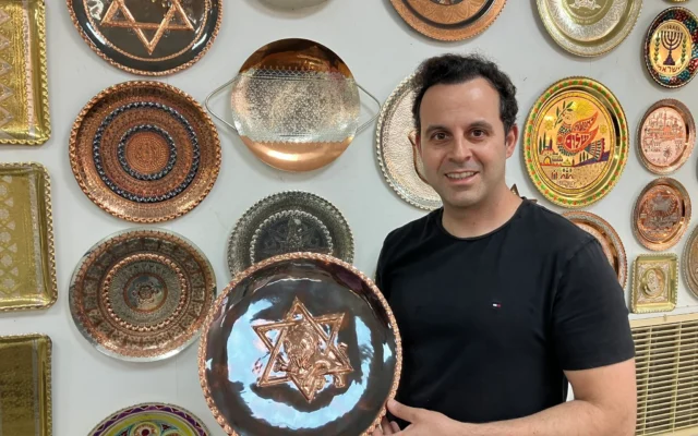 Le chaudronnier Dror Miro tient son assiette "Rising Lion"  qu'il a conçue et fabriquée dans la vieille ville d'Akko, le 16 juin 2025. (Crédit : Diana Bletter/Times of Israel)