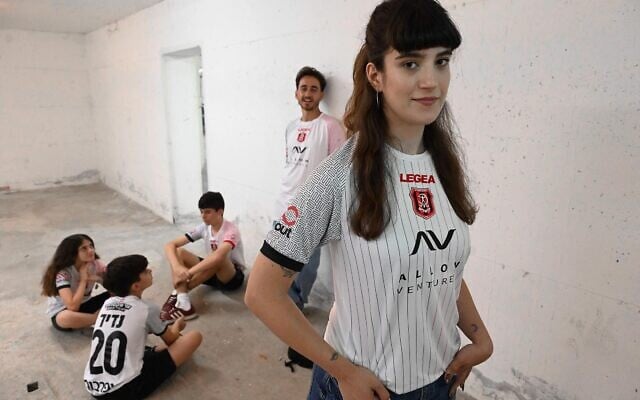 Des supporters du club de football Hapoel Jerusalem présentant leurs nouveaux maillots « extérieurs » dans un abri anti-bombes, signe des temps, le 17 juin 2025. (Crédit : Autorisation)