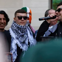 Le chanteur du groupe de rap irlandais Kneecap, Liam O'Hanna (au centre), qui se produit sous le nom de scène Mo Chara, devant le tribunal de Westminster à Londres le 18 juin 2025, après avoir été accusé de soutenir le Hezbollah. (Crédit : BENJAMIN CREMEL / AFP)