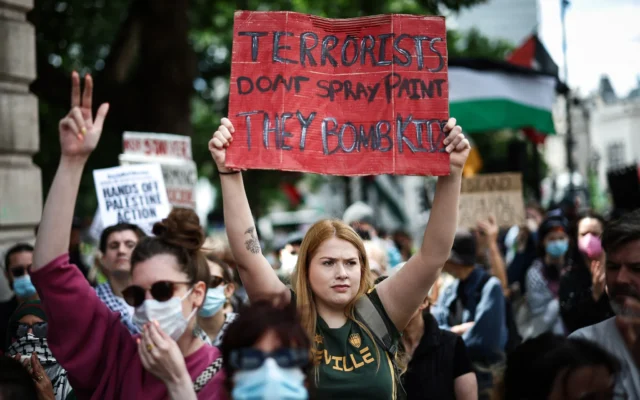 Un manifestant brandit une pancarte sur laquelle on peut lire « Les terroristes ne taguent pas, ils bombardent des enfants » lors d'un rassemblement en faveur du groupe pro-palestinien et anti-israélien Palestine Action, à Trafalgar Square, à Londres, le 23 juin 2025. (Crédit : Henry Nicholls / AFP) Un manifestant brandit une pancarte sur laquelle on peut lire « Les terroristes ne taguent pas, ils bombardent des enfants » lors d'un rassemblement en faveur du groupe pro-palestinien et anti-israélien Palestine Action, à Trafalgar Square, à Londres, le 23 juin 2025. (Crédit : Henry Nicholls / AFP)