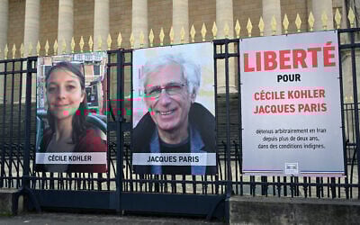 Les portraits de Cécile Kohler, actuellement emprisonnée en Iran, et de son compagnon Jacques Paris, ainsi qu'une pancarte indiquant "Liberté pour Cécile Kohler et Jacques Paris détenus arbitrairement en Iran depuis plus de deux ans dans des conditions épouvantables" devant le Palais Bourbon, l'Assemblée nationale française, à Paris, le 25 mars 2025. (Crédit : Bertrand Guay/AFP)