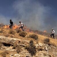 Des Palestiniens courant à travers une colline alors qu'ils tentent de chasser des résidents d’implantations violents dans le village de Sinjil, en Cisjordanie, le 4 juillet 2025. (Crédit : John Wessels/AFP)