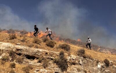 Des Palestiniens courant à travers une colline alors qu'ils tentent de chasser des résidents d’implantations violents dans le village de Sinjil, en Cisjordanie, le 4 juillet 2025. (Crédit : John Wessels/AFP)