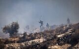 Des résidents d’implantations masqués lançant des pierres sur des Palestiniens depuis le sommet d'une colline, dans le village de Sinjil, en Cisjordanie, le 4 juillet 2025. (Crédit : John Wessels/AFP)
