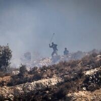 Des résidents d’implantations masqués lançant des pierres sur des Palestiniens depuis le sommet d'une colline, dans le village de Sinjil, en Cisjordanie, le 4 juillet 2025. (Crédit : John Wessels/AFP)
