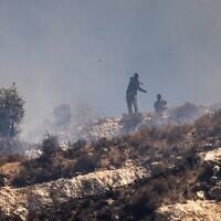 Des résidents d’implantations masqués lançant des pierres sur des Palestiniens depuis le sommet d'une colline, dans le village de Sinjil, en Cisjordanie, le 4 juillet 2025. (Crédit : John Wessels/AFP)