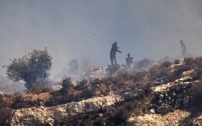 Des résidents d’implantations masqués lançant des pierres sur des Palestiniens depuis le sommet d'une colline, dans le village de Sinjil, en Cisjordanie, le 4 juillet 2025. (Crédit : John Wessels/AFP)
