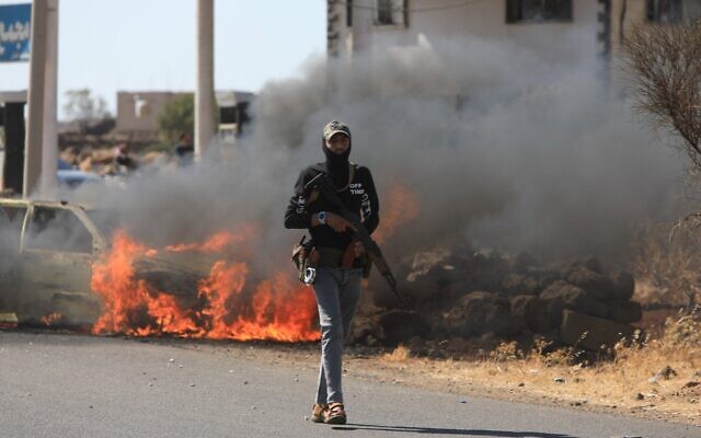 Un membre des forces de sécurité syriennes passant devant une voiture en feu dans le quartier de Mazraa, près de Soueïda, le 14 juillet 2025, à la suite d'affrontements entre des clans bédouins et des combattants locaux dans cette ville à majorité druze. (Crédit : Bakr Alkasem/AFP)