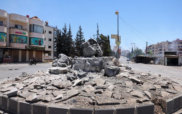 Des membres des forces de sécurité syriennes passent à moto devant un monument détruit dans la ville de Soueïda, à majorité druze, le 15 juillet 2025, à la suite d'affrontements entre des clans bédouins et des combattants druzes. (Crédit : Bakr Alkasem/AFP)