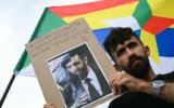 Un manifestant tient une pancarte indiquant « Le nouveau “président” de la Syrie était, est et restera un terroriste » devant un drapeau druze portant l'étoile druze lors d'une manifestation de soutien à la communauté druze syrienne, place du Trocadéro, à Paris, le 19 juillet 2025. (Crédit : Bertrand GUAY / AFP)
