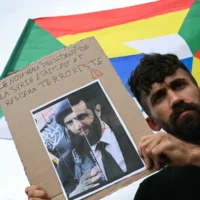 Un manifestant tient une pancarte indiquant « Le nouveau “président” de la Syrie était, est et restera un terroriste » devant un drapeau druze portant l'étoile druze lors d'une manifestation de soutien à la communauté druze syrienne, place du Trocadéro, à Paris, le 19 juillet 2025. (Crédit : Bertrand GUAY / AFP)