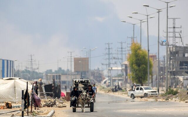 Un homme et une femme dans une charrette avec, à l'arrière-plan, la fumée dégagée par les frappes israéliennes, le long de la route de Salaheddin à Deir al-Balah, dans le centre de la bande de Gaza, le 21 juillet 2025. (Crédit : Eyad Baba/AFP) Un homme et une femme dans une charrette avec, à l'arrière-plan, la fumée dégagée par les frappes israéliennes, le long de la route de Salaheddin à Deir al-Balah, dans le centre de la bande de Gaza, le 21 juillet 2025. (Crédit : Eyad Baba/AFP)