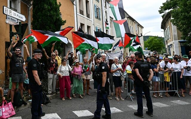 Des gendarmes français formant un périmètre tandis que des spectateurs brandissent des drapeaux "palestiniens" le long du parcours de la 17ᵉ étape de la 112ᵉ édition du Tour de France, entre Bollène et Valence, dans le sud de la France, le 23 juillet 2025. (Crédit : Loic Venance/AFP) Des gendarmes français formant un périmètre tandis que des spectateurs brandissent des drapeaux "palestiniens" le long du parcours de la 17ᵉ étape de la 112ᵉ édition du Tour de France, entre Bollène et Valence, dans le sud de la France, le 23 juillet 2025. (Crédit : Loic Venance/AFP)
