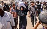 Une Palestinienne porte un sac de provisions sur sa tête dans le camp d'al-Mawasi, à Rafah, dans le sud de la bande de Gaza, le 27 juillet 2025. (Crédit : AFP)