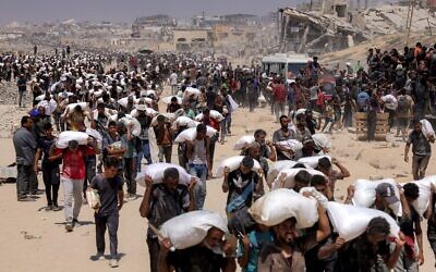 Des Gazaouis transportant des sacs de farine livrés après l'entrée de camions d'aide humanitaire en provenance du poste-frontière de Zikim, dans le nord de Gaza, le 27 juillet 2025. (Crédit : Bashar Taleb/AFP)