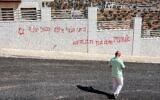 Un homme passant devant un graffiti israélien disant « Al-Mughayyir, tu le regretteras », après une attaque d'Israéliens radicaux contre le village chrétien de Taybeh, au nord-est de Ramallah, en Cisjordanie, le 28 juillet 2025. (Crédit : Zain Jaafar/AFP)