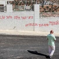 Un homme passant devant un graffiti israélien disant « Al-Mughayyir, tu le regretteras », après une attaque d'Israéliens radicaux contre le village chrétien de Taybeh, au nord-est de Ramallah, en Cisjordanie, le 28 juillet 2025. (Crédit : Zain Jaafar/AFP)
