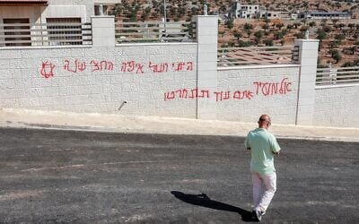 Un homme passant devant un graffiti israélien disant « Al-Mughayyir, tu le regretteras », après une attaque d'Israéliens radicaux contre le village chrétien de Taybeh, au nord-est de Ramallah, en Cisjordanie, le 28 juillet 2025. (Crédit : Zain Jaafar/AFP)